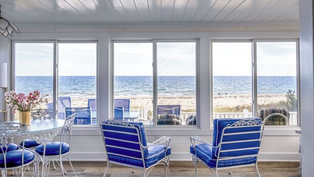 A room with a large window overlooking the beach, a table with chairs, and a decorative vase. - 93 Phillips Rd SD246 (Sagamore Beach)