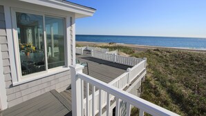 A coastal property with a wooden deck and a glass door leading to a patio area. - 93 Phillips Rd SD246 (Sagamore Beach)