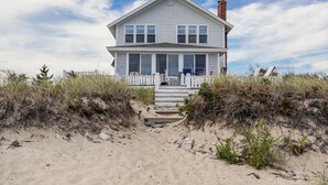 A two-story house with a front porch, located on a sandy beach with dunes. - 93 Phillips Rd SD246 (Sagamore Beach)