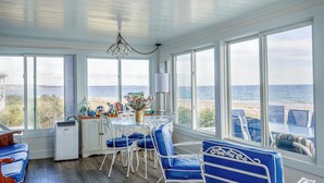 A sunroom with a view of the beach, a dining table with chairs, and a small kitchenette. - 93 Phillips Rd SD246 (Sagamore Beach)