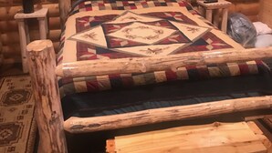 A log cabin room with a wooden bed, two bedside lamps, and a quilt. - Cabin 2 (Garden City)