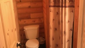 A wooden cabin bathroom with a toilet, a shower curtain, and a door. - Cabin 2 (Garden City)