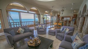 A spacious living area with a large coffee table, sofas, and a view of the ocean through arched windows. - Beachfront Delfin Estate with Pool (Sleeps 41) (Mazatlán)