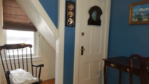 Une pièce avec un fauteuil à bascule en bois, une porte blanche, une petite table et un tableau accroché au mur.
