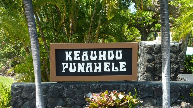A sign with the text "KEARUHU PUNAHELE" in a brown frame, surrounded by tropical vegetation and a stone wall.