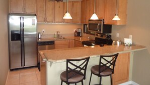 A modern kitchen with wooden cabinets, stainless steel appliances, a central island with bar stools, and pendant lighting.