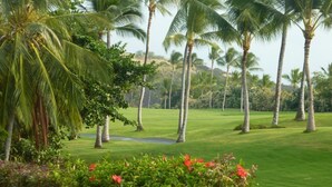 A lush green golf course with palm trees and red flowers in the foreground.