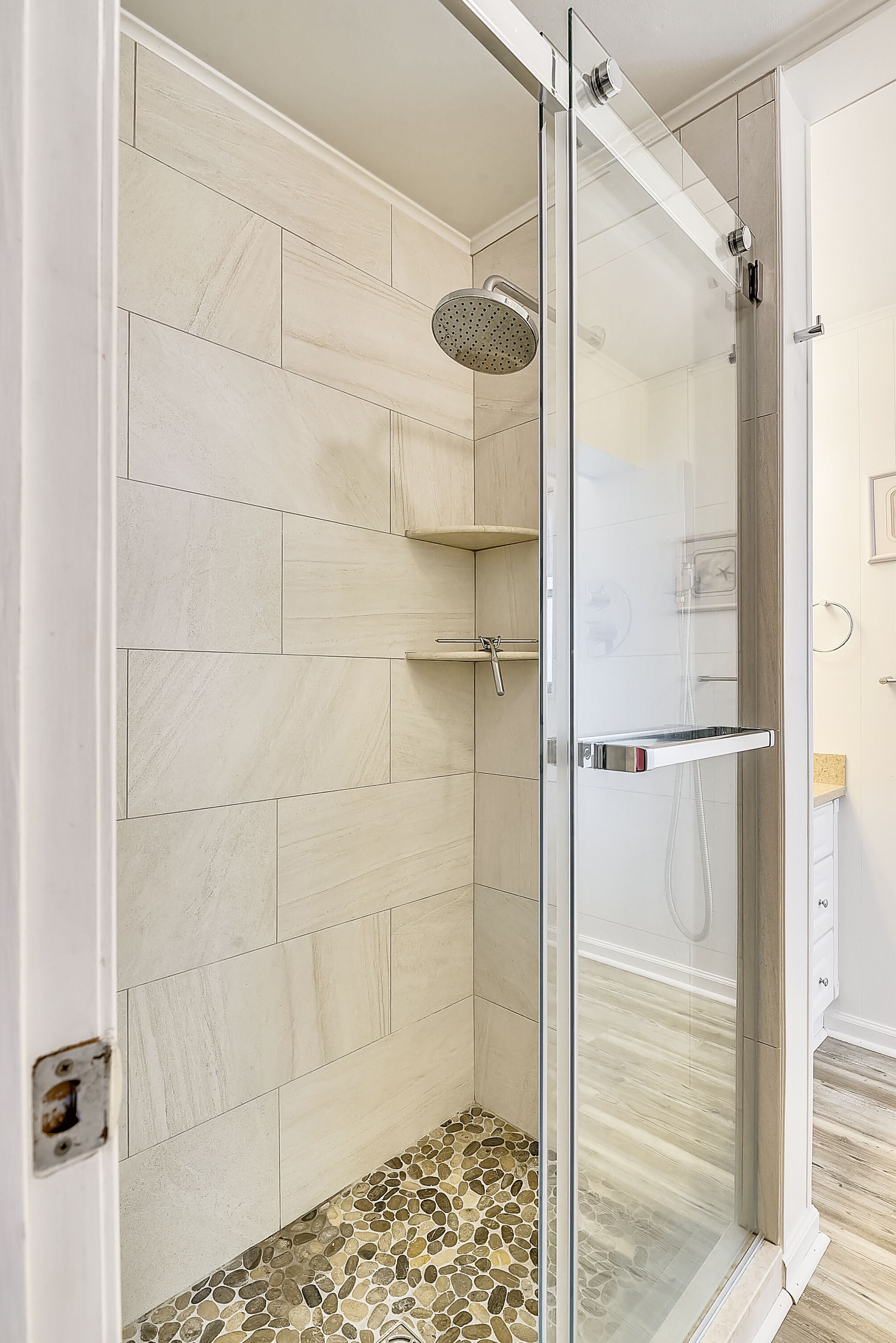 Une douche moderne dotée d’une porte en verre, de murs carrelés et d’un sol en mosaïque.