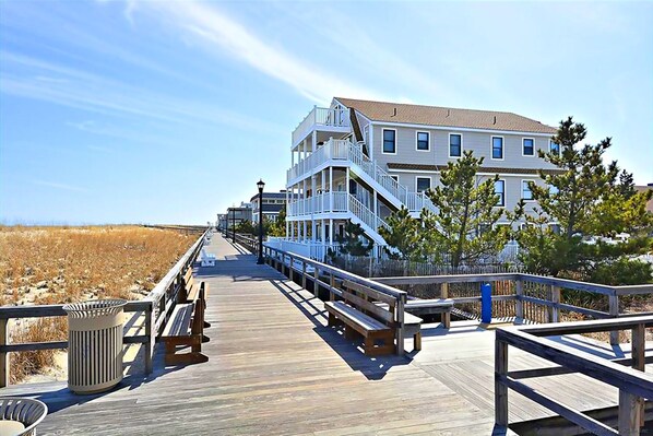A wooden boardwalk leading to a multi-story building with balconies, situated near a beach. - Oceanfront, Pristine 1br 1 Ba Condo, Relax And Rejuvenate By The Sea. (Bethany Beach)