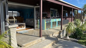 Um deck de madeira com área de churrasco, porta de vidro e vista para o interior.