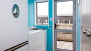 Uma cozinha compacta com máquina de lavar, pia e janela com vista para um deck de madeira.