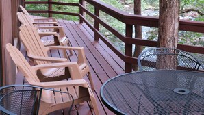 Une terrasse en bois, avec des chaises et une table en métal, entourée d’arbres.
