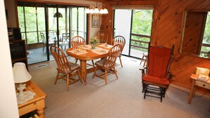 Un intérieur en bois comprenant une table à manger, des chaises, un téléviseur et de grandes fenêtres.