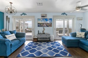 A living room with two blue sofas, a patterned rug, a TV, and a balcony with a view of the beach. - Reef on the Beach (Corpus Christi)
