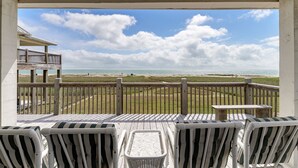 Een balkon met uitzicht op het strand, met gestreepte stoelen en een tafeltje.