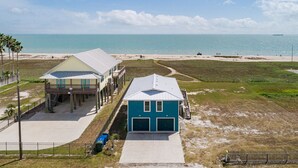 Een gebouw met twee verdiepingen, een garage en een overdekt terras, naast een strand met uitzicht op de oceaan.