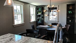 Een moderne keuken met een marmeren aanrecht, zwarte stoelen, een eettafel en een kroonluchter met zichtbare lampen.