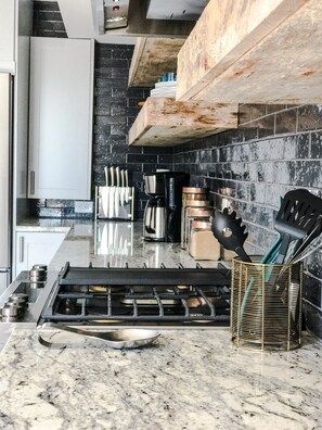 A kitchen with a gas stove, black tiled backsplash, and stainless steel appliances.