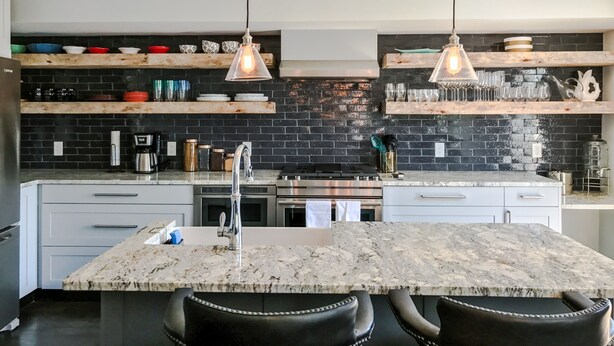 Een moderne keuken met een marmeren eiland, een backsplash van zwarte baksteen en hangende lampen.