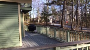 Eine Holzterrasse mit grüner Geländer, einem überdachten Grillbereich und Blick auf bewaldetes Gelände.