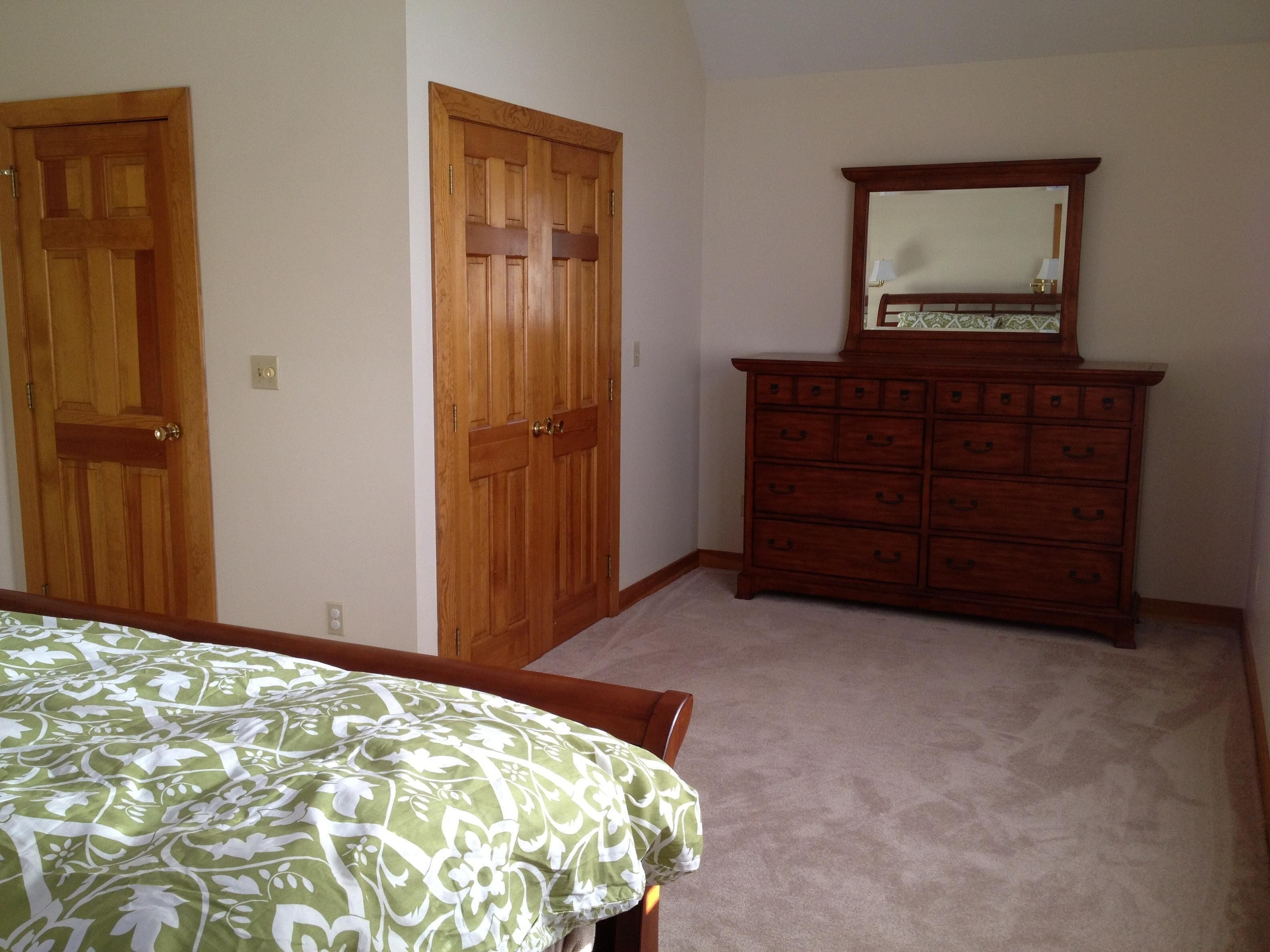 A bedroom with a bed, two wooden doors, a dresser, and a mirror.