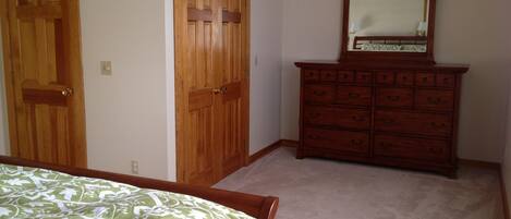 A bedroom with a bed, two wooden doors, a dresser, and a mirror.