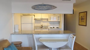Una cocina compacta con refrigerador, microondas, estufa y pileta. Se observa un pequeño comedor con una silla y mesa.
