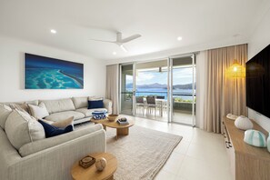 A modern living room with a sofa, coffee table, and a large painting of a coastal scene. - Lagoon 204 - Hamilton Island (Whitsundays)