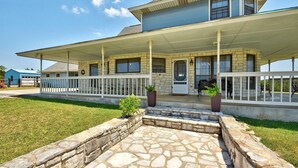 A two-story house with a stone foundation, a covered porch with white railings, and a stone patio in front.