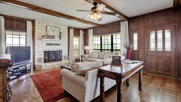 A spacious living room with a fireplace, wooden beams, a large window, and a door with stained glass.