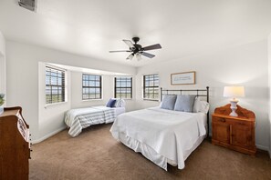 A bedroom with two beds, a ceiling fan, a bedside table with a lamp, and a window with blinds. - Prosit Ranch - 300 Acre Private Ranch w/360 Degree Views & Wrap-Around Porch (Wimberley)
