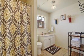 A bathroom with a patterned shower curtain, a toilet, a sink with a mirror, and a towel rack with folded towels. - Prosit Ranch - 300 Acre Private Ranch w/360 Degree Views & Wrap-Around Porch (Wimberley)