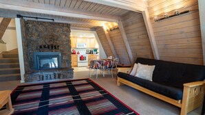 A cozy loft-style living area with a stone fireplace, a black sofa, and a dining table with chairs.