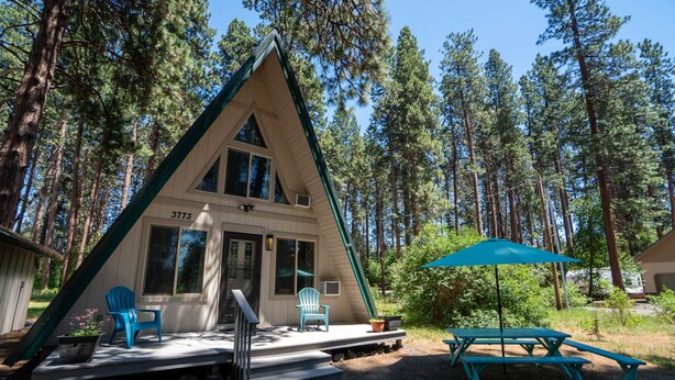 A cabin with a triangular roof, a porch with steps, and a picnic table with an umbrella.