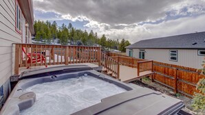 A hot tub in a backyard with a wooden deck, a wooden fence, and a building in the background.