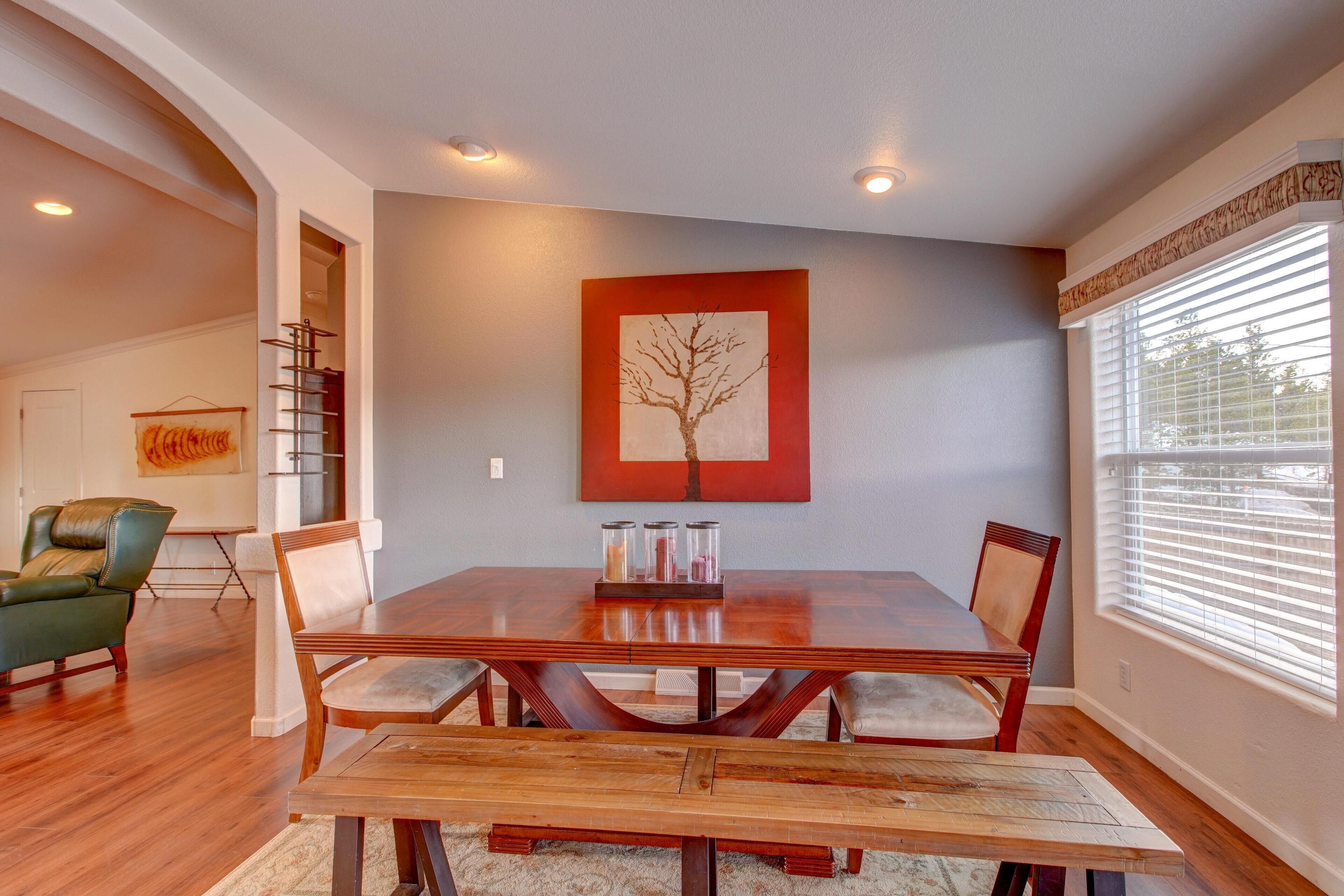 A dining area with a wooden table and chairs, a painting on the wall, and a window with blinds.