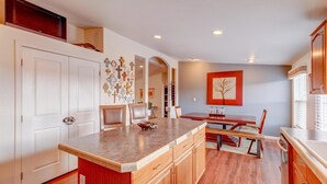A modern kitchen with a central island, wooden cabinets, and a dining area with a red accent wall.