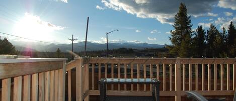 A wooden deck with a bench and railing, overlooking a mountainous landscape with a clear sky.