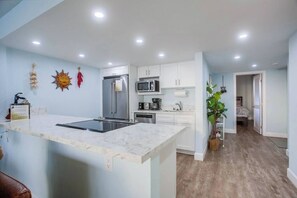 A modern kitchen with a central island, built-in appliances, and a view into a bedroom.