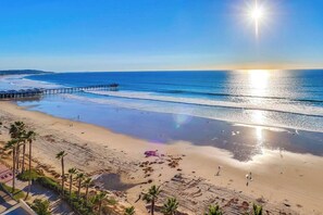 Una spiaggia con un molo che si protende nell'acqua, palme e cielo sereno.