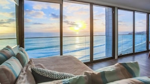 A room with a large window overlooking the ocean, a sofa with cushions, and a view of the sunset.