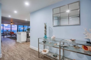 A modern kitchen with a glass display case containing decorative shells, a large window overlooking a balcony, and a view of the ocean.