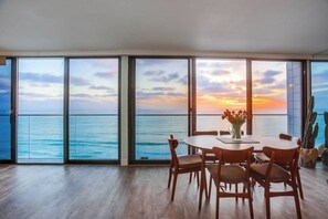 A dining area with a view of the ocean and sunset through large windows.