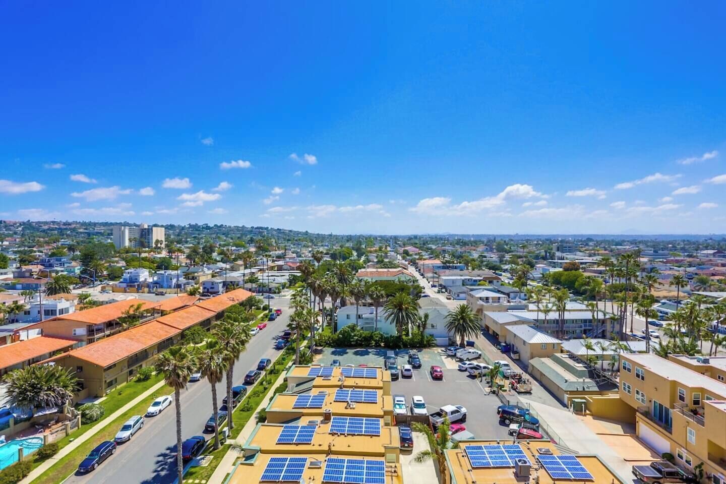 A residential area with multiple-story buildings, a parking lot with cars, and solar panels on rooftops.
