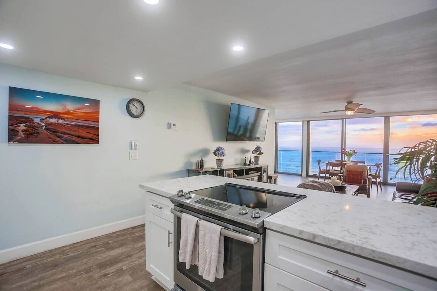 A modern kitchen with a built-in stove, a dining area with a view of the sea, and a large painting on the wall.
