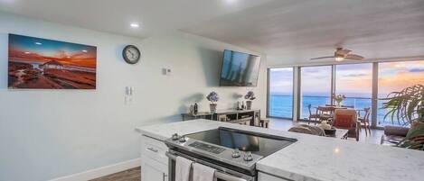 A modern kitchen with a built-in stove, a dining area with a view of the sea, and a large painting on the wall.