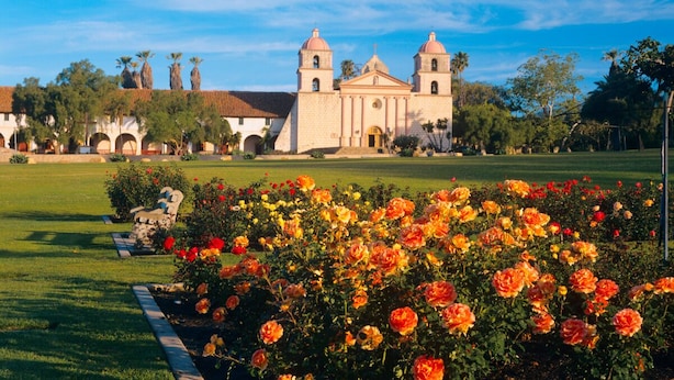 A historic building with two towers, surrounded by a well-maintained garden with vibrant flowers.