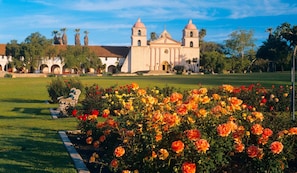 A historic building with two towers, surrounded by a well-maintained garden with vibrant flowers.