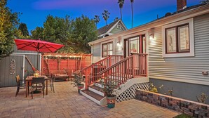 A patio with a dining table and chairs, a red umbrella, and potted plants.