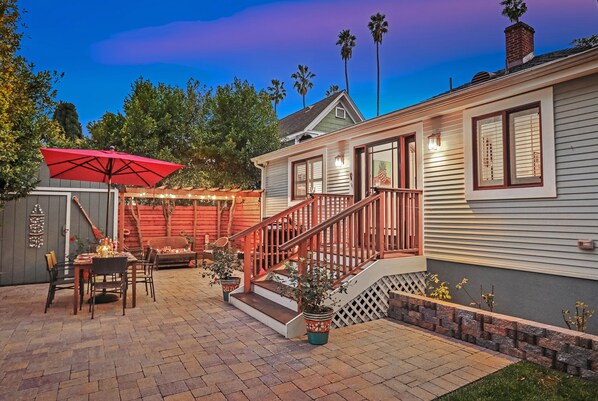 A patio with a dining table and chairs, a red umbrella, and potted plants.